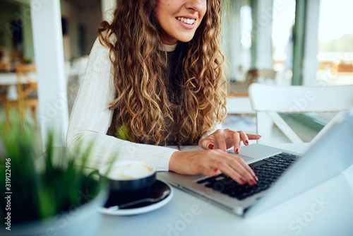 Attractive young curly brunette enjoying her coffee/tea and working on laptop 