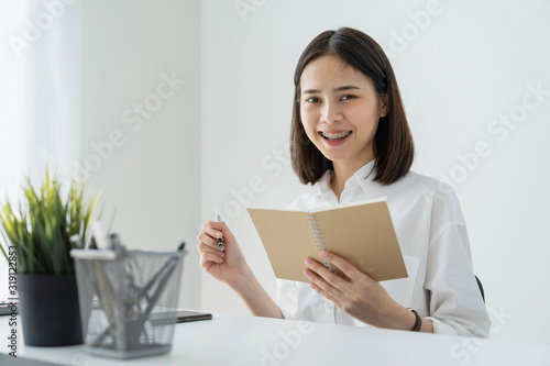 Woman holding blank notebook and pen on table in office.