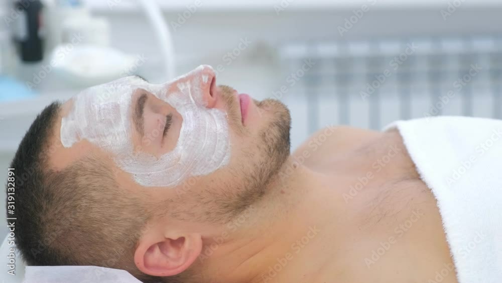 Young man with closed eyes and white mak on face lying on couch in beauty clinic, spa procedure. Relaxing, waiting time, face closeup, side view. Beauty industry concept. Guy enjoying in cosmetology. Young man with closed eyes and white mak on face lying on couch in beauty clinic, spa procedure. Relaxing, waiting time, face closeup, side view. Beauty industry concept. Guy enjoying in cosmetology.