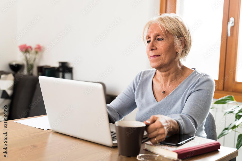 retired woman holding a cup of coffee working at home retired woman holding a cup of coffee working at home