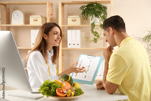Young nutritionist consulting patient at table in clinic photo