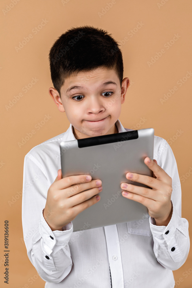 Little surprised boy using tablet on light yellow studio background. Little surprised boy using tablet on light yellow studio background.