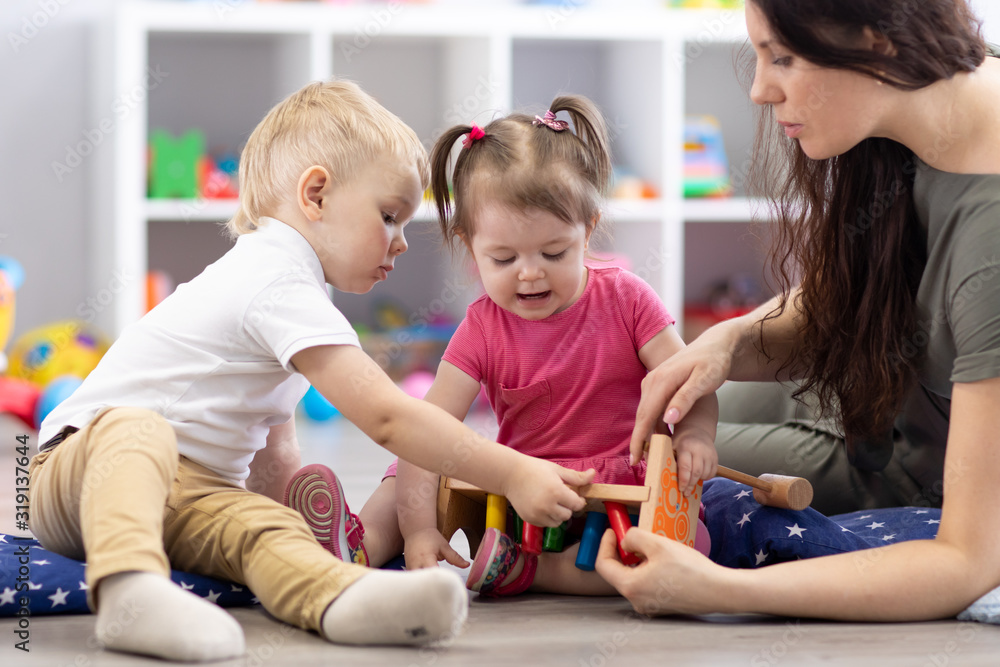 Preschooler children playing with educational wooden toys at kindergarten or daycare center. Toddlers with teacher in nursery. Preschooler children playing with educational wooden toys at kindergarten or daycare center. Toddlers with teacher in nursery.