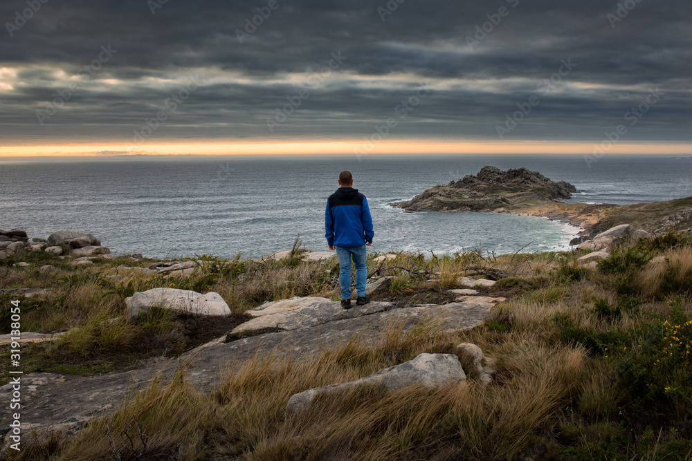 Man watching the horizon on the coast. The ruins that can be seen are of the Castro de Baroña, a pre-Roman settlement, which today is an important tourist attraction in the area. Galicia, Spain.