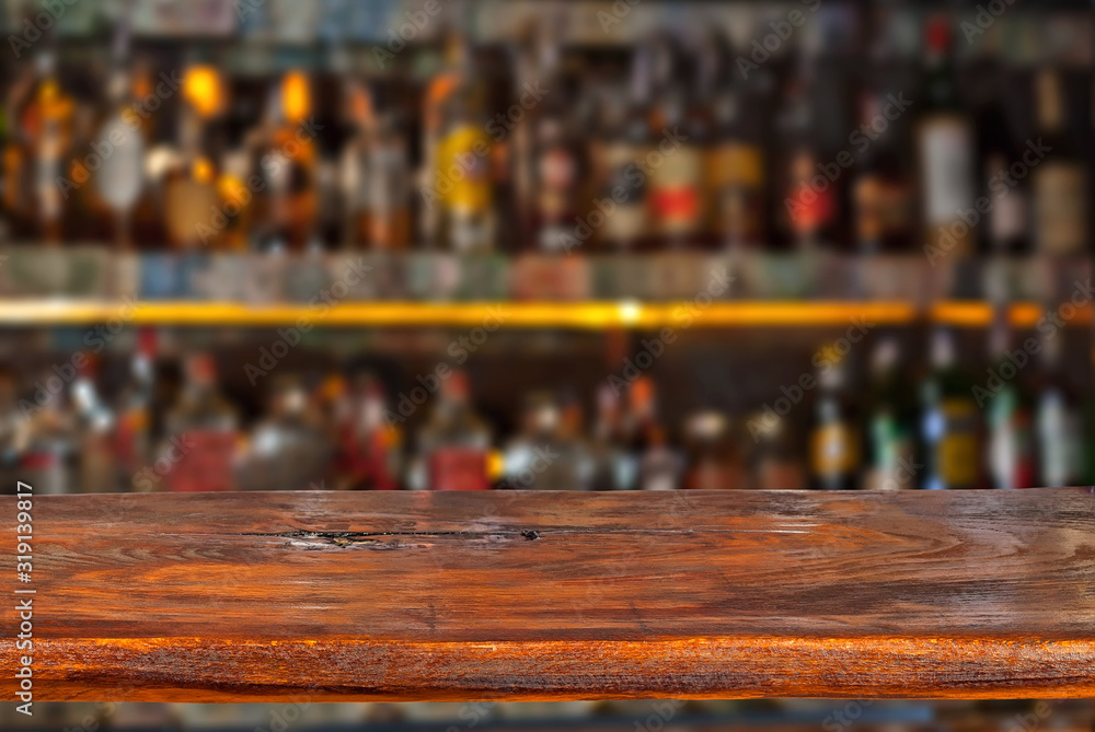 Wooden board on a background of bottles with alcohol. Old bar counter as layout for design. Workpiece for design. Empty place to advertise products. Blurred interior of the bar in the background. Wooden board on a background of bottles with alcohol. Old bar counter as layout for design. Workpiece for design. Empty place to advertise products. Blurred interior of the bar in the background.