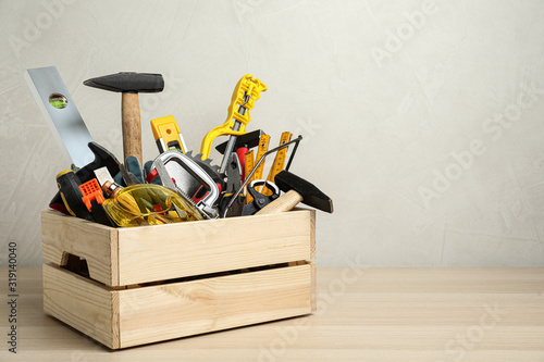 Crate with different carpenter's tools on wooden table. Space for text photo