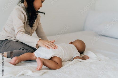 Careful Asian girl in casual wear patting newborn baby caring child with little brother lying on bed in flat