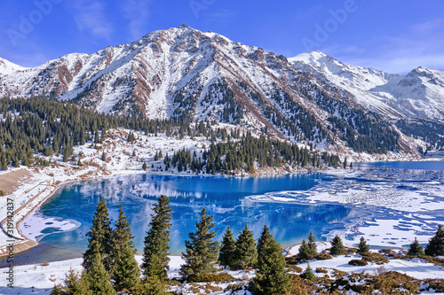 Autumn gives way to winter, air temperature drops and the water in the lake begins to freeze. Texture and patterns of ice on the serene water surface of a mountain lake; Big Almaty lake in Kazakhstan