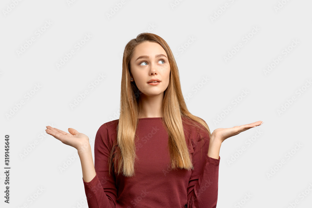 Thoughtful girl spreads hands in different directions. Beautiful young woman wears Burgundy-colored jacket sleeves isolated on white background in Studio with an empty space for text and advertising. Thoughtful girl spreads hands in different directions. Beautiful young woman wears Burgundy-colored jacket sleeves isolated on white background in Studio with an empty space for text and advertising.
