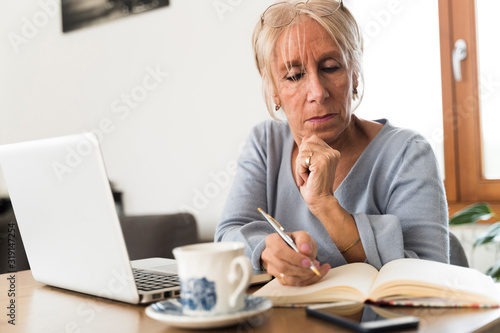 Serious adult woman writing and working with a laptop at home