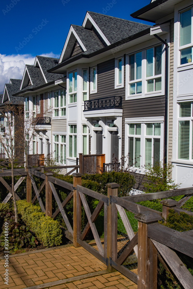 Row of new townhomes in a sidewalk neighborhood. On a sunny day in spring against bright blue sky.