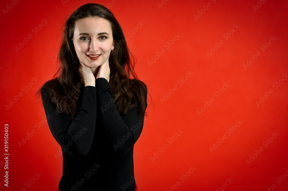 Fototapeta premium Photo of a pretty young brunette woman with a smile with good makeup on a red background. Concept girl talking in front of the camera with emotions.