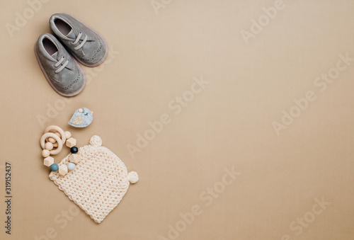 Baby wooden teether, knitted hat and shoes on beige background