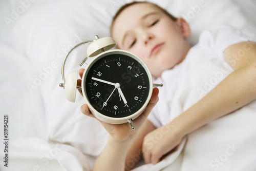 cute little boy hand turned off alarm clock on bed in sunlit, sleep and relaxation concept.