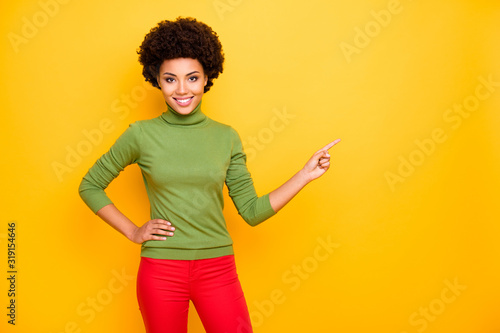 Photo of cheerful positive pretty cute girlfriend pointing into empty space at sales in red pants isolated vivid color background