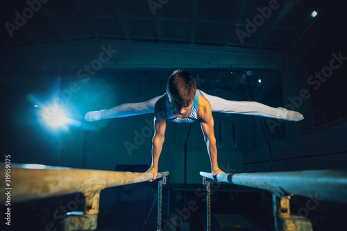 Little male gymnast training in gym, flexible and active. Caucasian fit little boy, athlete in white sportswear practicing in exercises for strength, balance. Movement, action, motion, dynamic concept