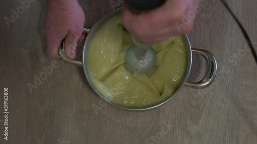 Man in the kitchen Making vegetable cream with hand mixer.  Zenith view