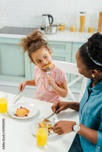 african american mother looking at daughter eating tasty pancakes