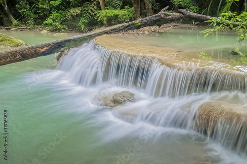 Fototapeta Naklejka Na Ścianę i Meble -  Beautiful silky water cascade flowing on cliff rocks around with blue-green water and green forest background, Erawan Waterfalls, 1th step, Kanchanaburi, west of Thailand.