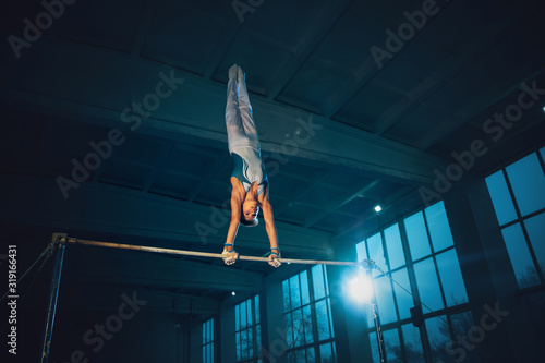 Little male gymnast training in gym, flexible and active. Caucasian fit little boy, athlete in white sportswear practicing in exercises for strength, balance. Movement, action, motion, dynamic concept