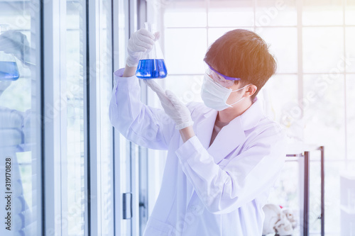 Male scientist looking at flask with blue liquid..