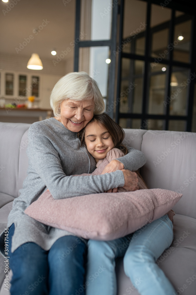 Grandmother hugging tightly granddaughter sitting on the couch. Grandmother hugging tightly granddaughter sitting on the couch.