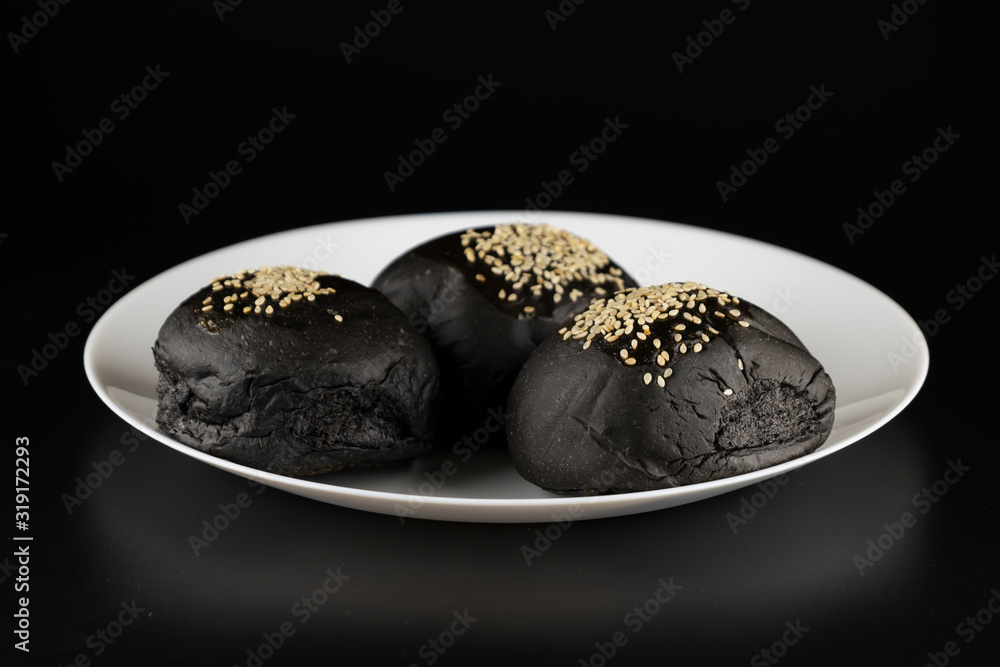 Loaf of charcoal bread bun with white sesame on top in the white plate isolated on black background