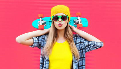 Portrait cool woman with skateboard wearing colorful yellow hat on pink background