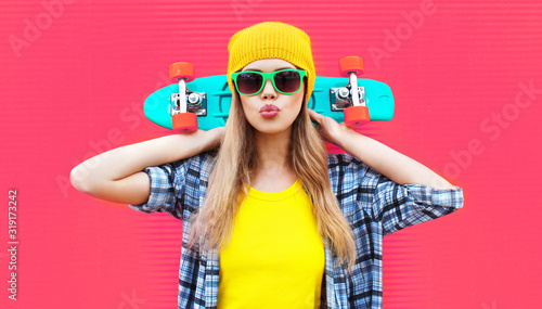 Portrait cool woman with skateboard wearing colorful yellow hat on pink background photo