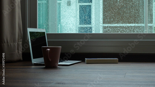 computer notebook next to a cup coffee on rainy day window background
