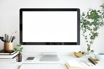 Modern personal computer with blank white screen, keyboard, mobile phone and office accessories on desk at workplace of graphic designer, blogger. Electronic devices, technology and creativity