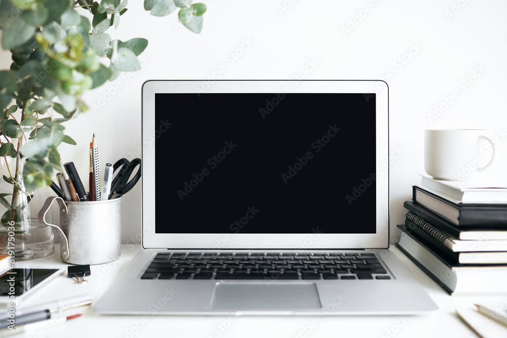 Fototapeta premium Modern cozy workplace of student with laptop computer with copy space display, textbooks and stationary accessories on white desk. Interiors, design, style, technology and education concept