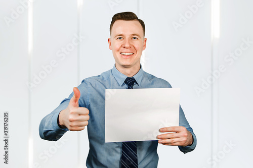 Young guy businessman dressed in blue shirt and tie holding blank blank sheet of paper a4