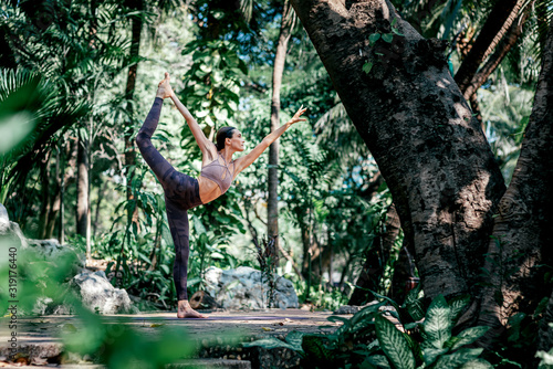 Transforming energy. Full-length shot of caucasian woman standing in Dancer's pose, Natarajasana while practicing yoga outdoors, in a garden. Healthy lifestyle and relaxation concept
