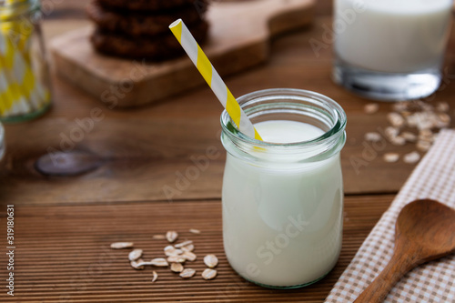 Glass jar, bottle of oat milk with paper straw on wooden background with copy space.
