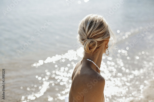 Back view of blonde hairdo and necklace on the naked shoulders near the sea on the sunny summer day