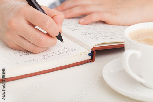 Female hands writing in leather bound journal or diary with coffee