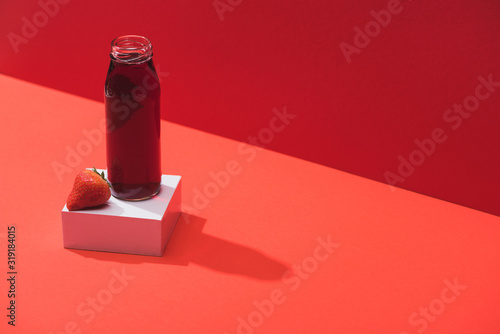 fresh berry juice in glass bottle near ripe strawberry on cube on red background © LIGHTFIELD STUDIOS