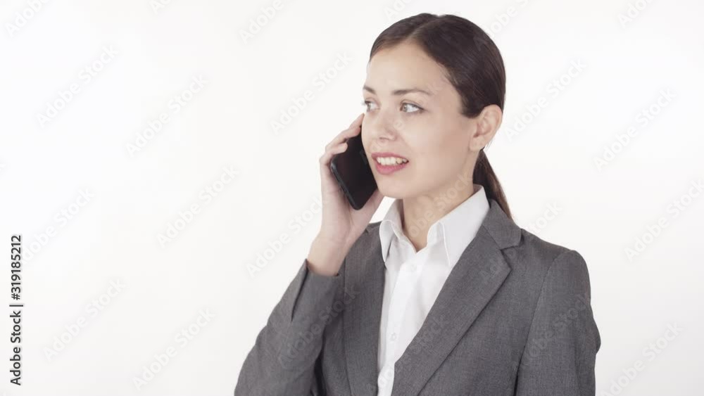 Close up portrait of young beautiful businesswoman wearing shirt and jacket standing against white wall while having telephone conversation Close up portrait of young beautiful businesswoman wearing shirt and jacket standing against white wall while having telephone conversation