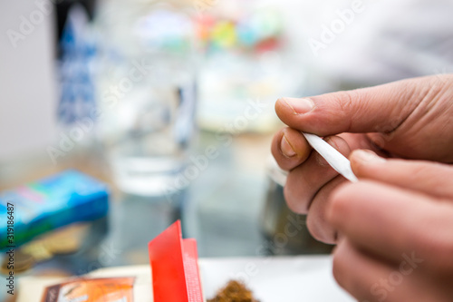 Closeup on the hands of a man who just wraps a tobacco cigarette and a sheet of paper by hand. In the background you can see an ashtray and spilled tobacco. Copy Space.