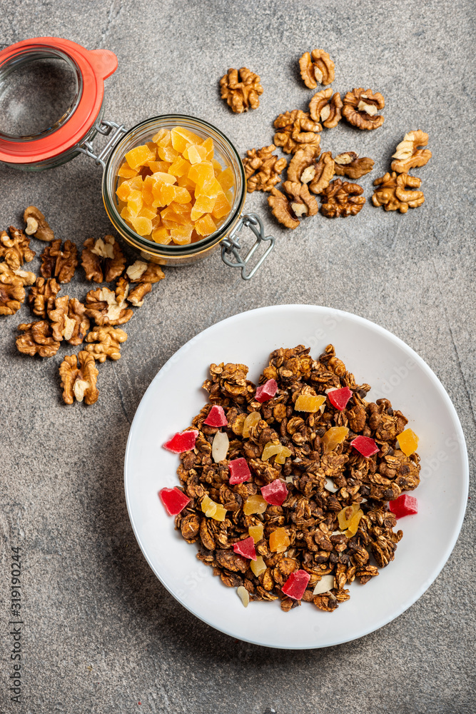 Fototapeta premium Granola with dried fruits in a white plate on a gray background. Close-up. Open decorative jar with dried fruits. Top view.