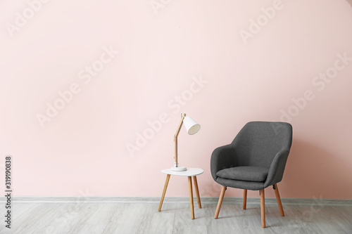 Stylish armchair with table and lamp near color wall in room
