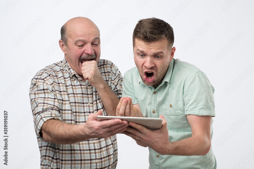 Φωτογραφία Caucasian mature father and son looking in internet for the latest news using electronic tablet