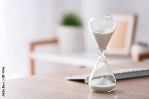 Hourglass with computer keyboard on table in office. Time management concept