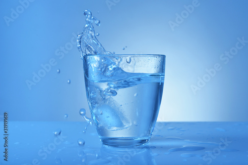 Glass of fresh water with splash on color background