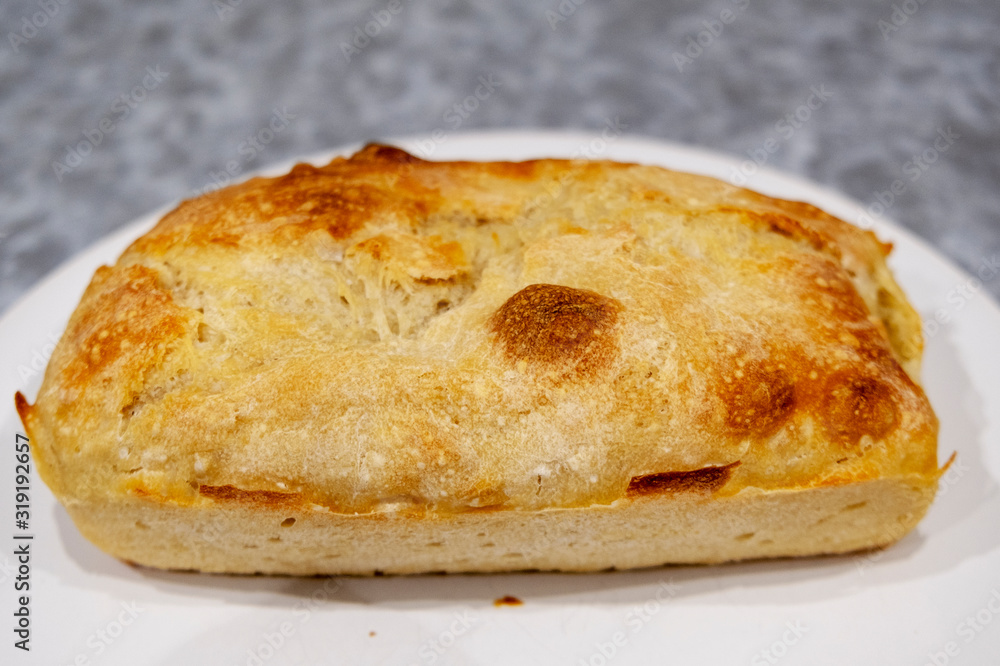 homemade bread with a crisp crust lies on a white plate.