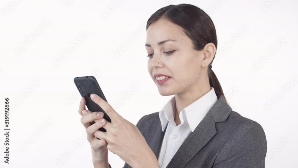 Close up of young beautiful woman wearing shirt and jacket using smartphone while standing against white background Close up of young beautiful woman wearing shirt and jacket using smartphone while standing against white background
