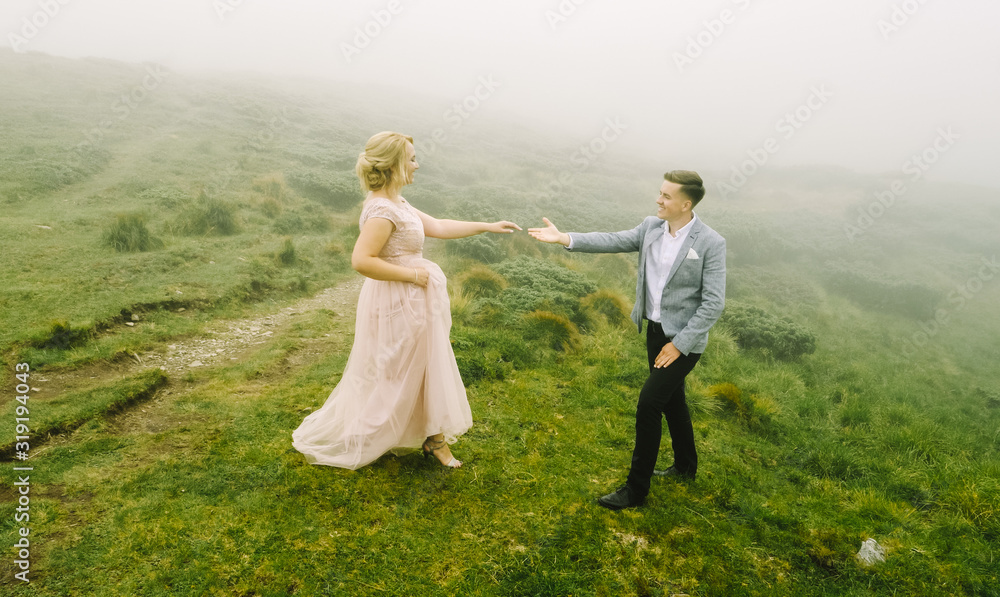 Luxury couple in evening dresses are hugging on the mountain meadow