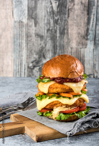 Homemade chicken burger with fried egg tomato lettuce cucumber dripping mozzarella on cutting board vertical orientation. Copy space photo