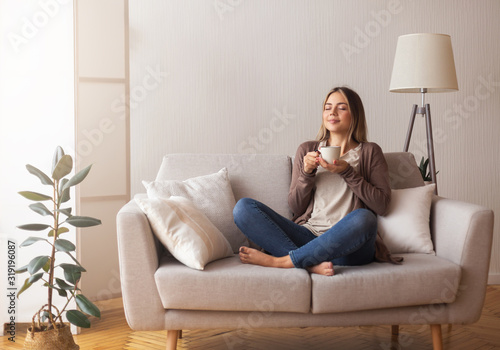 Young coffee lover sniffing hot drink at cozy home interior